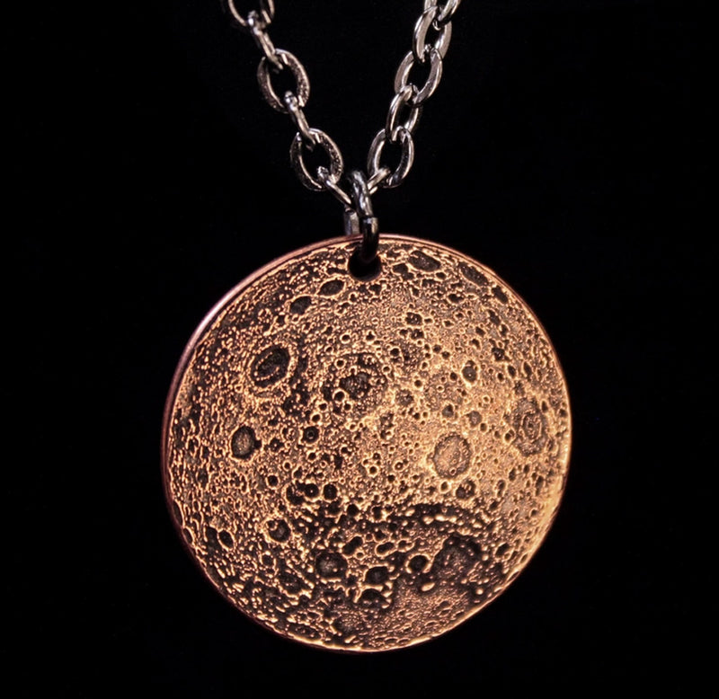 The back side of a copper necklace pendant depicting the moon. 