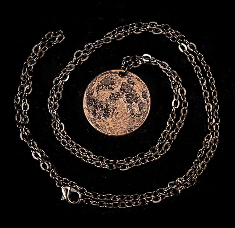 A copper moon pendant with the necklace chain coiled around it. 