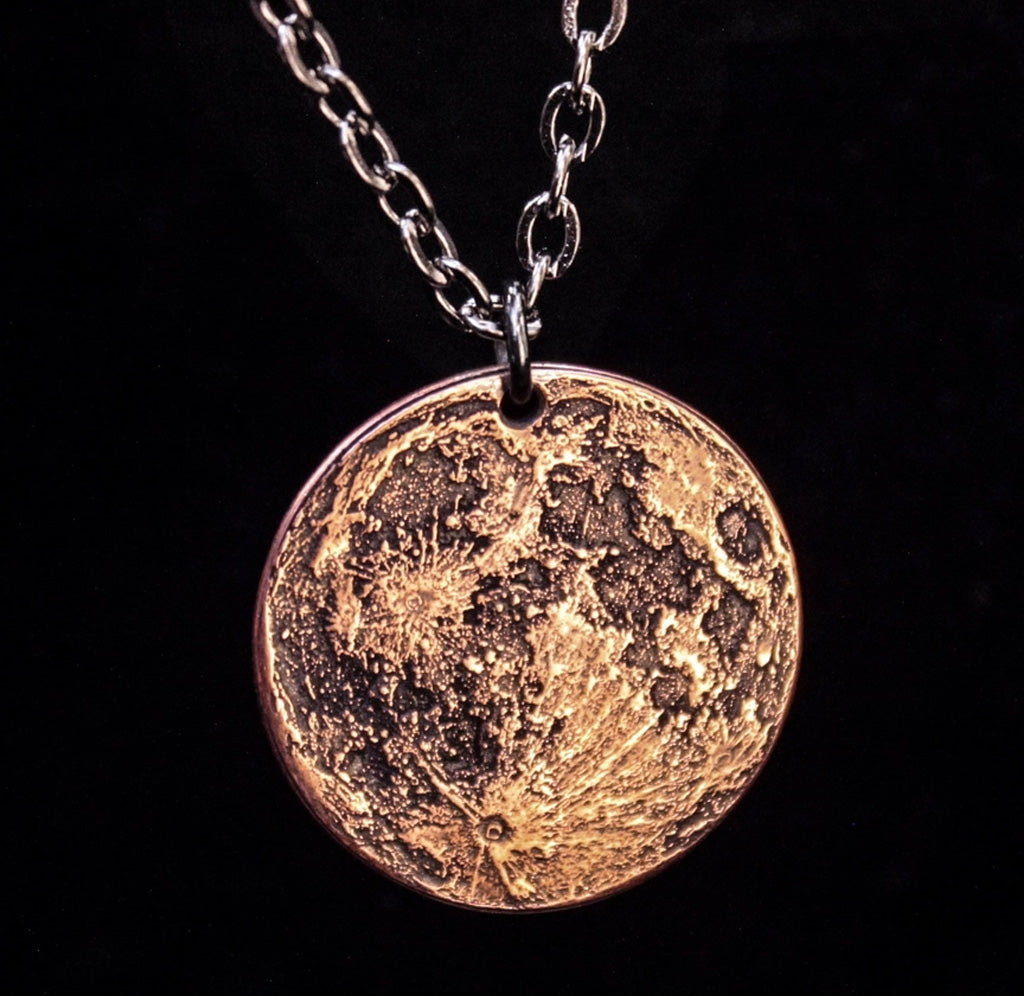 The front side of a copper necklace pendant depicting the moon. 