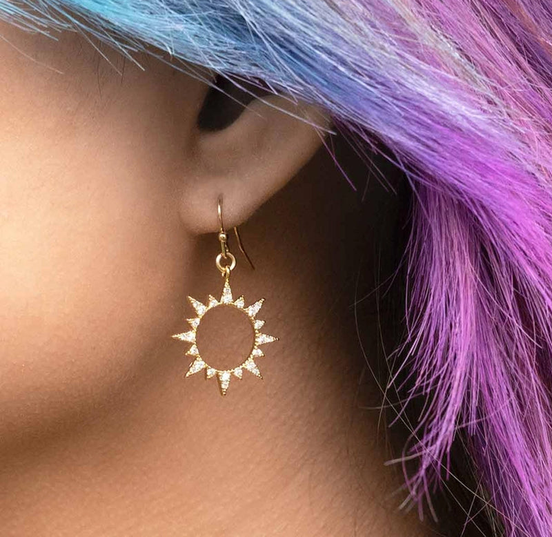 A close up image of an ear with the dangling sun earring being worn. 