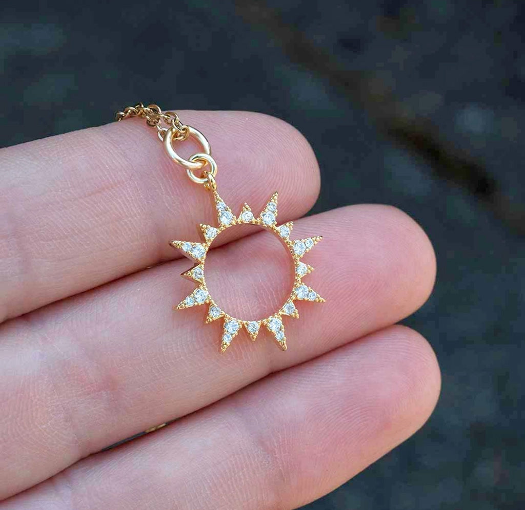 A hand is holding the sun shaped pendant necklace. 