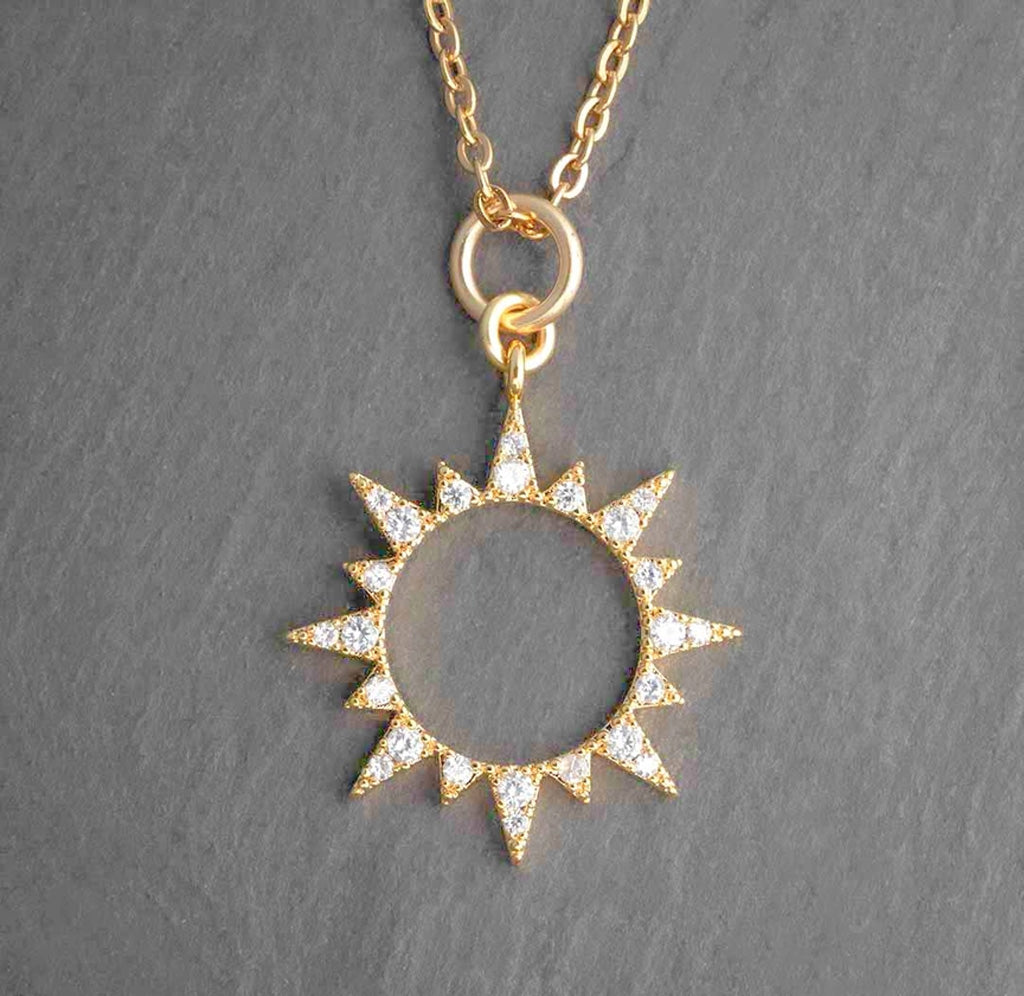 A gold colored sun pendant with a hollow center. The rays have white crystals studded on them. 