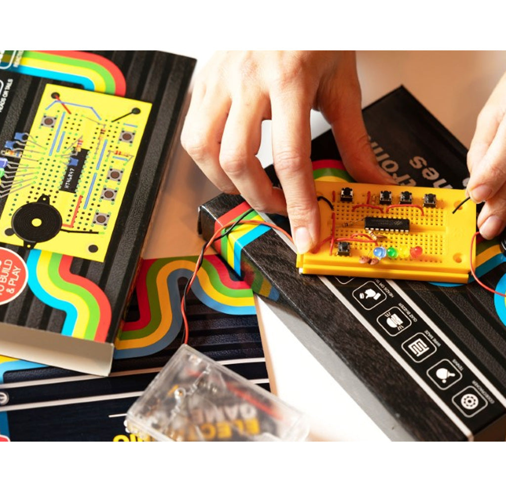 A table with open packaging and two hands working on a yellow circuit board.