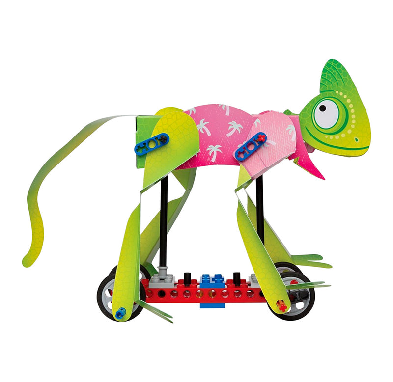 A green chameleon wearing a pink shirt is constructed with paper and attached to a red platform with four wheels on the bottom. Each leg of the chameleon is attached to a wheel. 