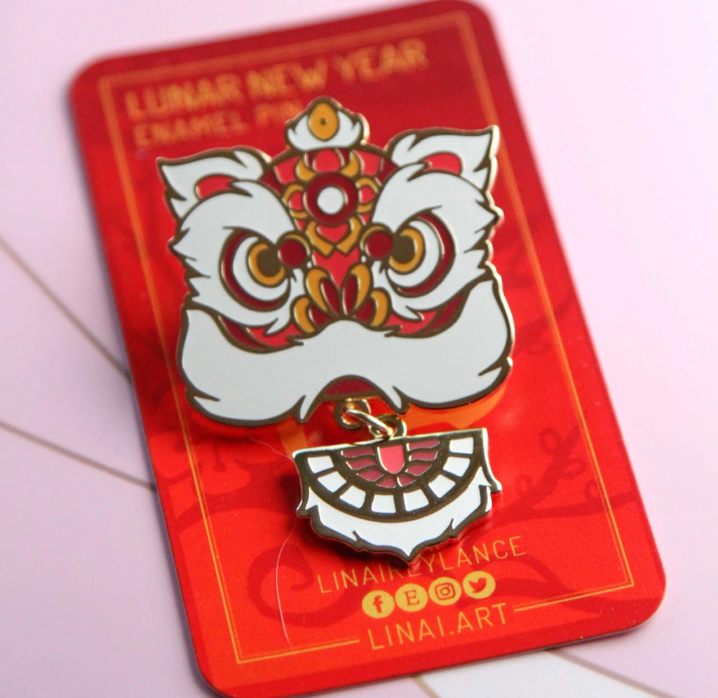 A red and white enamel pin in the shape of a lions head. The pin is mounted on a red card. 