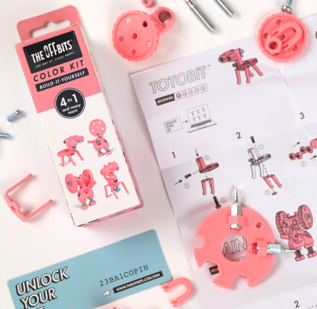 The pink package is pictured with pink gears and screws from the package scattered around. There is an instruction sheet depicting building instructions and a blue sheet of paper with a code. 