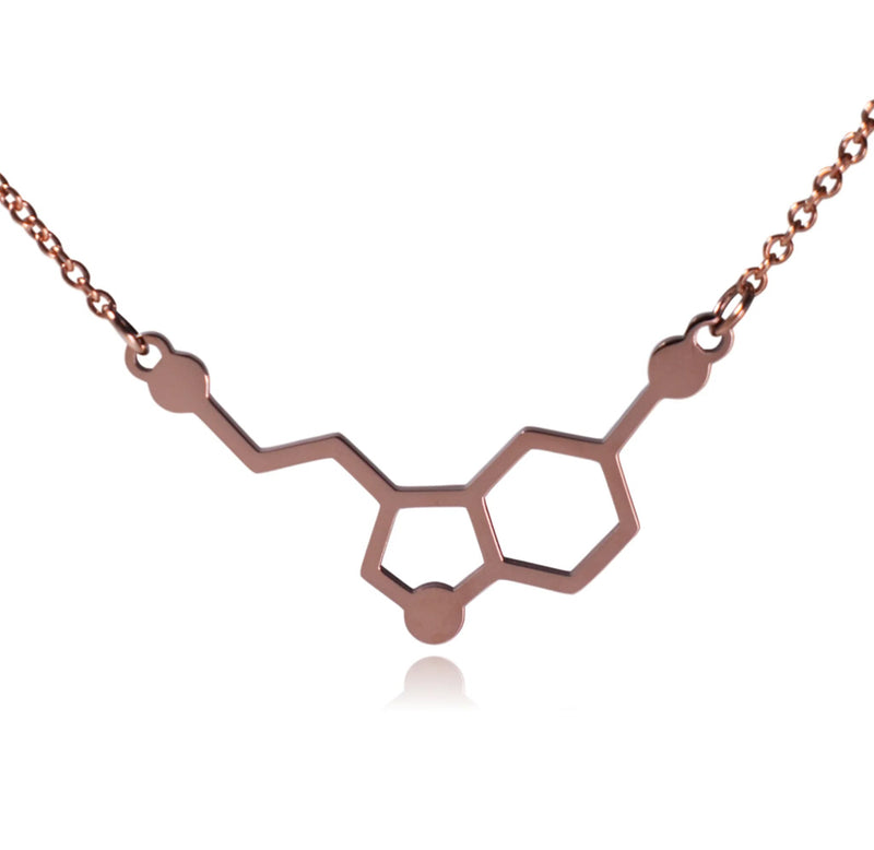 a rose gold colored metal charm shaped with two hexagons, a few bent lines, and circles (the shape of serotonin's molecular structure). 