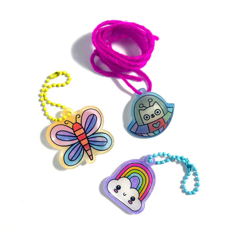 three charms are displayed -- a cat in a UFO, a butterfly, and a rainbow with a cloud. Each charm is colored in and attached to yarn or a chain. 