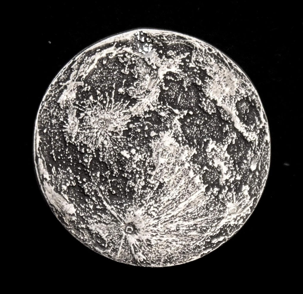 Silver colored moon coin showing shaded regions of the moon. 