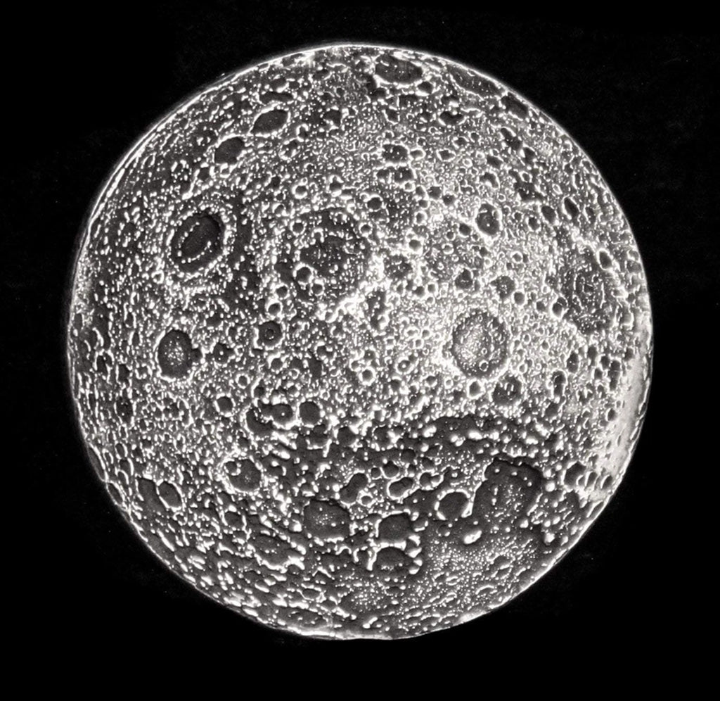 Silver colored moon coin showing dotted regions of the moon. 