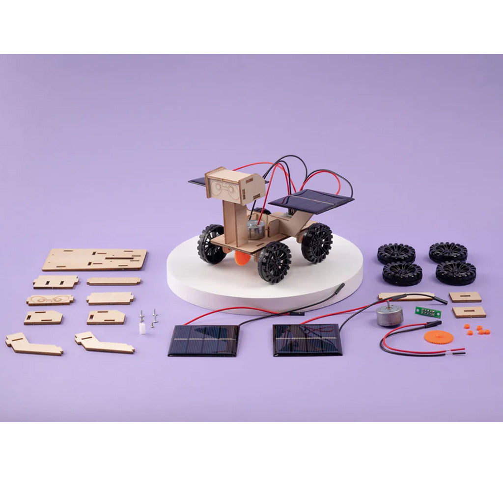 Laser cut wood pieces, two solar panels, red and black wire, black plastic wheels, and a few other parts are laid out neatly around a constructed rover.