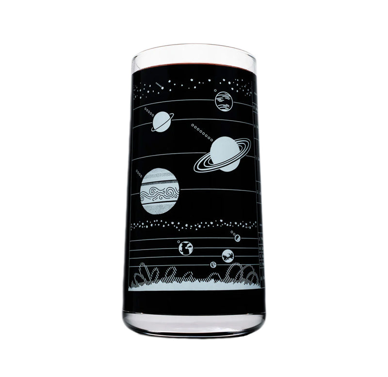 A drinking glass with white lines depicting the planets in the solar system. The glass is filled with a dark liquid. 